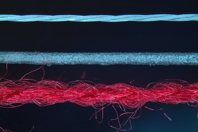 A highly magnified color image of three different textile fibers, one red, two blue.