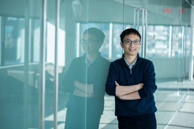 Photo of Yichen Shen leaning against an opaque cyan-colored glass wall with his arms folded