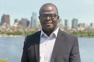 Photo of Carl Dey smiling and standing in front of the Charles River