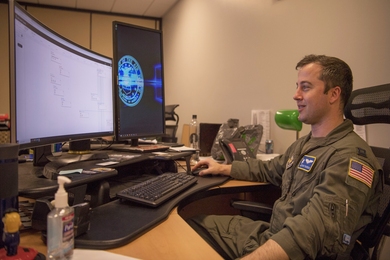 Photo of an air force pilot in an office looking at a computer monitor.