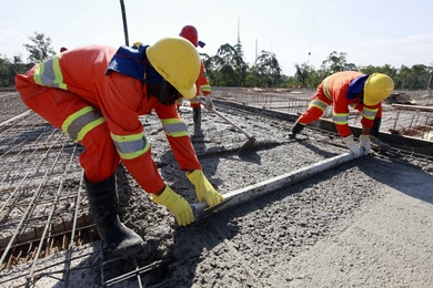 Photo of three workers in orange jumpsuits and yellow hard hats laying concrete.