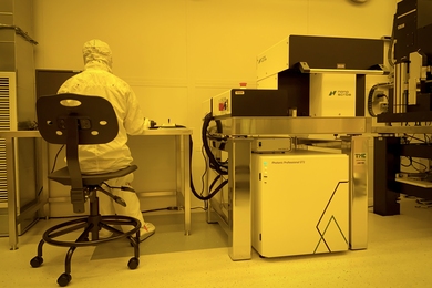 Yellow-tinted photo of a researcher in a clean suit using a large piece of lab equipment