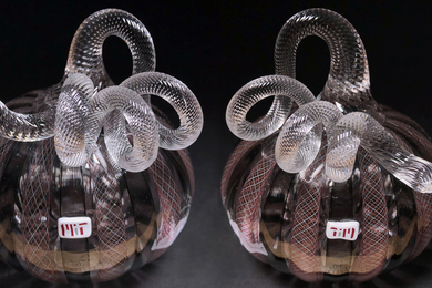 Photo of two glass pumpkins with very curvy stems. They are both primarily clear glass with stripes that include some crimson, and each has a glass "MIT" logo attached