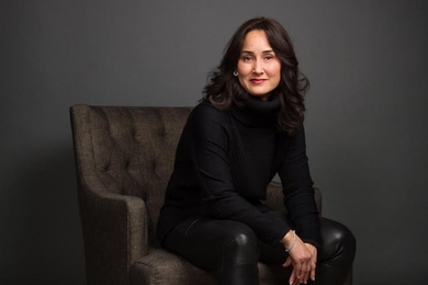 Portrait photo of Cynthia Breazeal, seated, wearing black clothes against a dark background