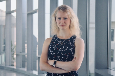 Photo of Mariya Greenberg, standing in front of a window with her arms crossed
