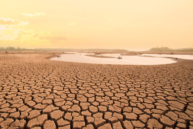 Photo of a dried-up lakebed with cracked mud taking up most of the scene, with a small pond of water in the distance