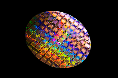 Photo of a rainbow-colored circular wafer containing integrated circuits against a black background