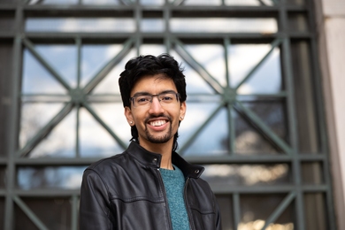 Photo of a student standing with an MIT wall of windows behind him.