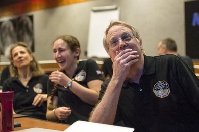 Photo of Richard Binzel is in focus with his hand covering his mouth as he looks at something off-camera in amazement. Behind him are two other people out of focus, one of whom is laughing.