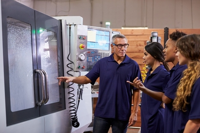 Photo of an instructor standing with trainees in front of a Computer Numerical Control (CNC) machine