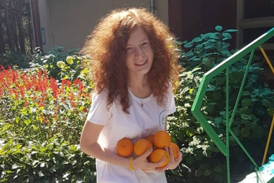 Photo of Yulia Zdanovska standing in front of a garden, holding oranges.