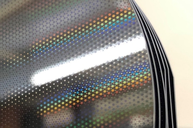 Photo of a stack of shiny silicon mirrors. The top one is coated with etching patterns featuring repeating small circles. Some are rainbow colored when catching the ambient light.