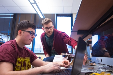 Lecturer Joe Steinmeyer leans over a student's keyboard to point to a section of computer monitor.