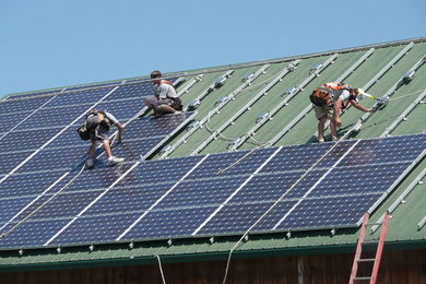 Photo of three workers installing solar panels on a pitched roof