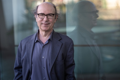 Photo of Frank Wilczek standing in front of a building, his profile reflected in the glass behind him.