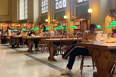 Photo of Milain Fayulu reading in a library with a high arched ceiling and windows