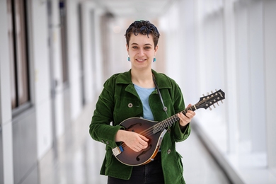 Photo of Zoe Levitt standing in the center of the frame in a white hallway, holding a mandoline and smiling.