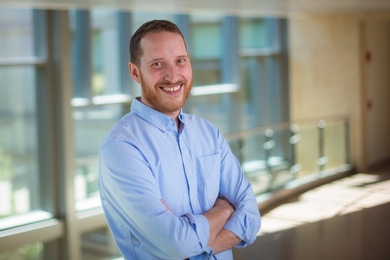 Portrait photo of Noah Nathan standing in front of a wall of windows