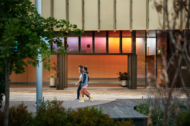 Three MIT community members walk by the colorful MIT Illuminations lighting display at the MIT Welcome Center