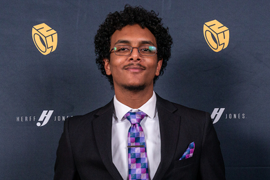 Headshot of Mohamed Magdi Taha standing in front of a backdrop featuring simplified illustrations of the MIT Brass Rat class ring