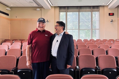 Jesus Sotomayor and David Nino stand together in an empty lecture hall, laughing together. Sotomayor has his hand on Nino’s shoulder.