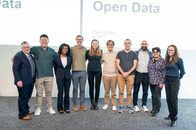 Ten people stand in a line with their arms around each other and smile.