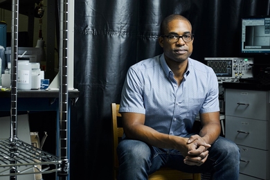 Photo of a man in a shortsleeve button-down shirt sitting in a lab with his hands folded, looking at the camera