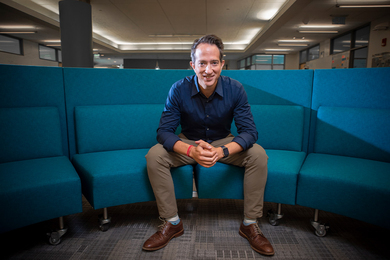 Jason Jay sits on a curved blue sectional couch inside an office