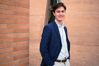 Julian Zulueta stands outside wearing a button-up shirt and blazer, with the brick walls of Stata in background. 