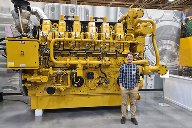 Photo of Santiago Andrade standing in front of a large yellow machine in a warehouse.