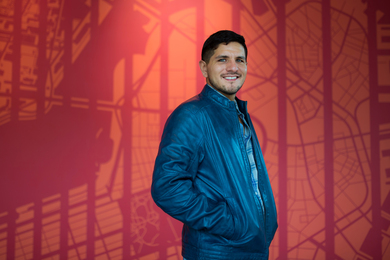 Flavio Emilio Vila Skrzypek smiles and stands in front of a red and orange map covering a wall.