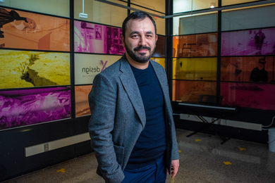 Cagri Zaman stands in front of colorfully illustrated wall panels.