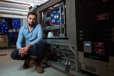 Florian Chavagnat inside a lab with instruments in the background; he is squatting down to pose in front of a lab workbench with shelves