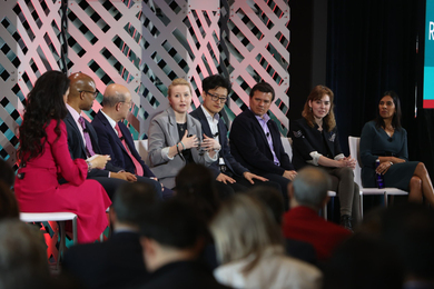 A moderator and seven MIT faculty members sit on stage. Professor Anne White, in the center, is speaking while the others look on.