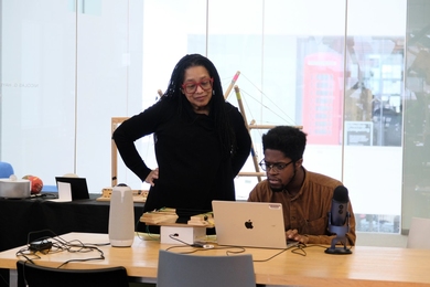 Pamela Z standing next to a seated man working on a laptop