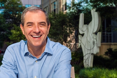 Portrait photo of David Autor in front of Pablo Picasso’s abstract cement sculpture Figure découpée in an outdoor courtyard
