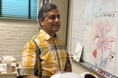Abhay Ram stands in front of a whiteboard, holding an open physics textbook.