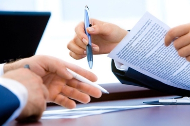 A closeup photo of two sets of hands. Both hold pens, and one holds a piece of paper.