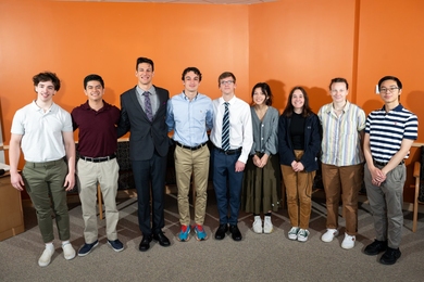 Nine interns pose for a group photo in front of an orange wall. 