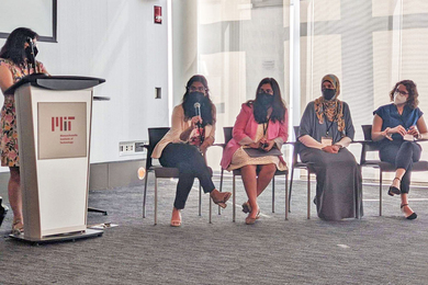 Panel discussion with one individual standing at a lectern and four others seated. All are wearing face masks.