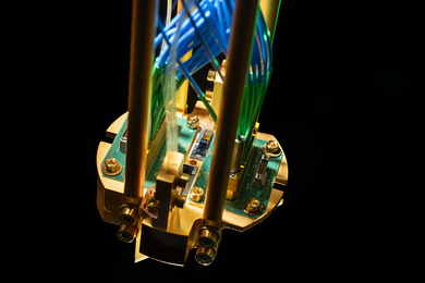 Close-up photo of a quantum repeater module mounted on a gold-plated copper assembly and connected to green printed circuit boards, with optical fibers routed up.