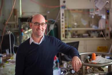 Professor Jesse Kroll stands beside gas equipment in his lab.