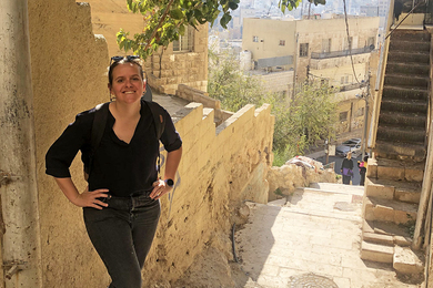 Elizabeth Parker-Magyar poses at the top of an ancient-looking stone staircase overlooking many old buildings in Amman, Jordan