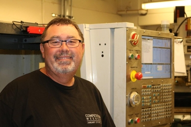 Pat McAtamney smiles in front of a large machine inside a cement brick room
