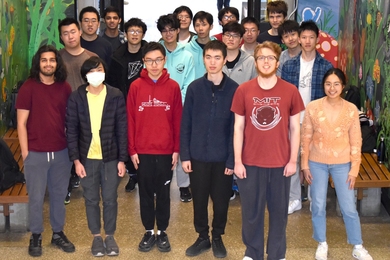 19 students standing a group with colorful mural walls behind them