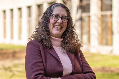 Closeup photo of Julie Greenberg on a sunny day with a brick building behind her