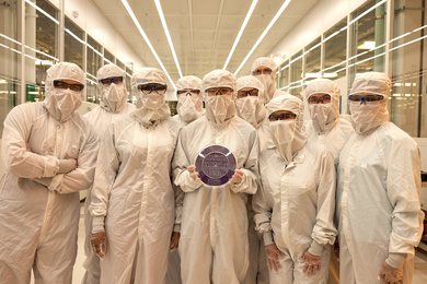 Ten people clad in white protective clothing covering all but their eyes, which are behind safety glasses, pose as a group inside a nanotechnology cleanroom.