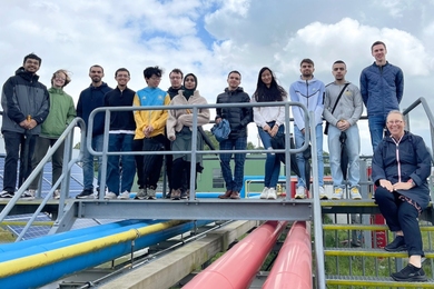 13 people pose together on a catwalk over hydrogen pipelines