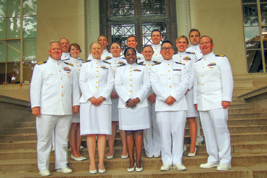 Fourteen graduates wear white navy uniforms on the steps of Building 5.