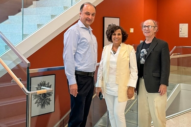 Vladimir Bulović, Denise Milan, and Frank Wilczek pose together in front of a staircase, with framed artwork on the walls.